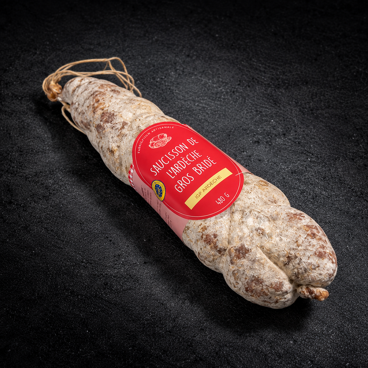 Gros saucisson bridé de l'Ardèche IGP 480 g, ficelé à la main, avec son étiquette, sur fond d'ardoise noire