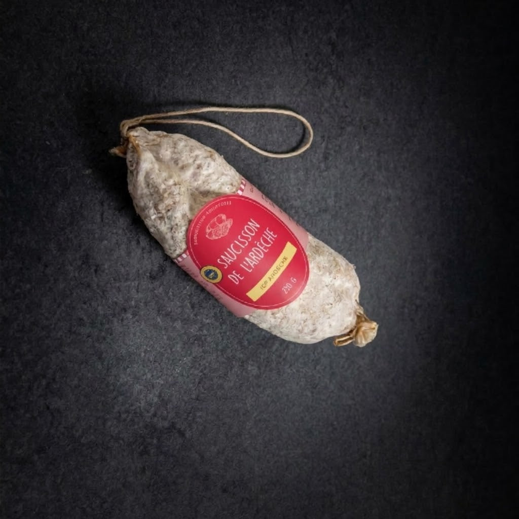 Ganze Trockenwurst aus der Ardèche g.g.A. mit Etikett und Aufhängeschnur, von oben auf dunklem Hintergrund
