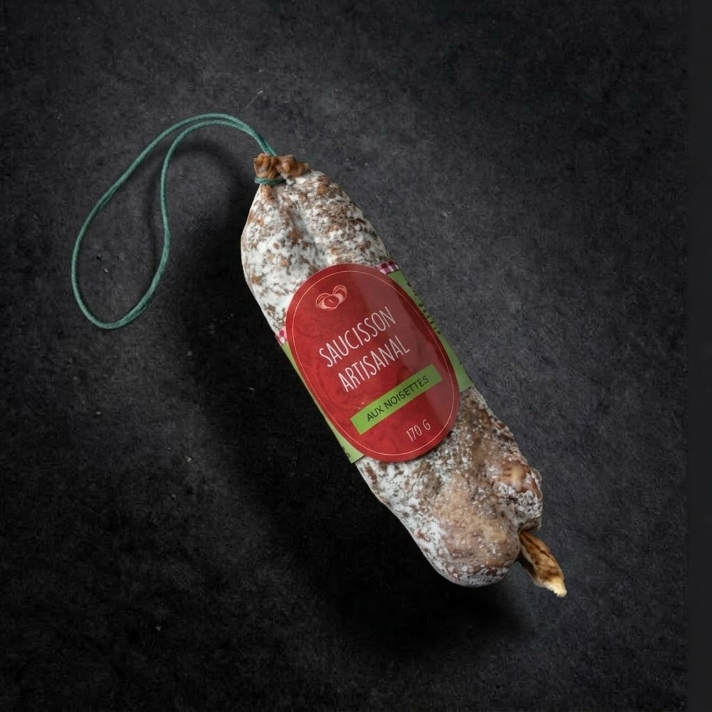 Saucisson sec artisanal aux noisettes 170 g avec sa ficelle verte et son étiquette, sur fond d'ardoise noire